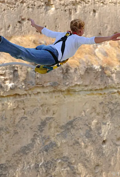 Woman with Bungee cord jumping off ledge with arms wide open