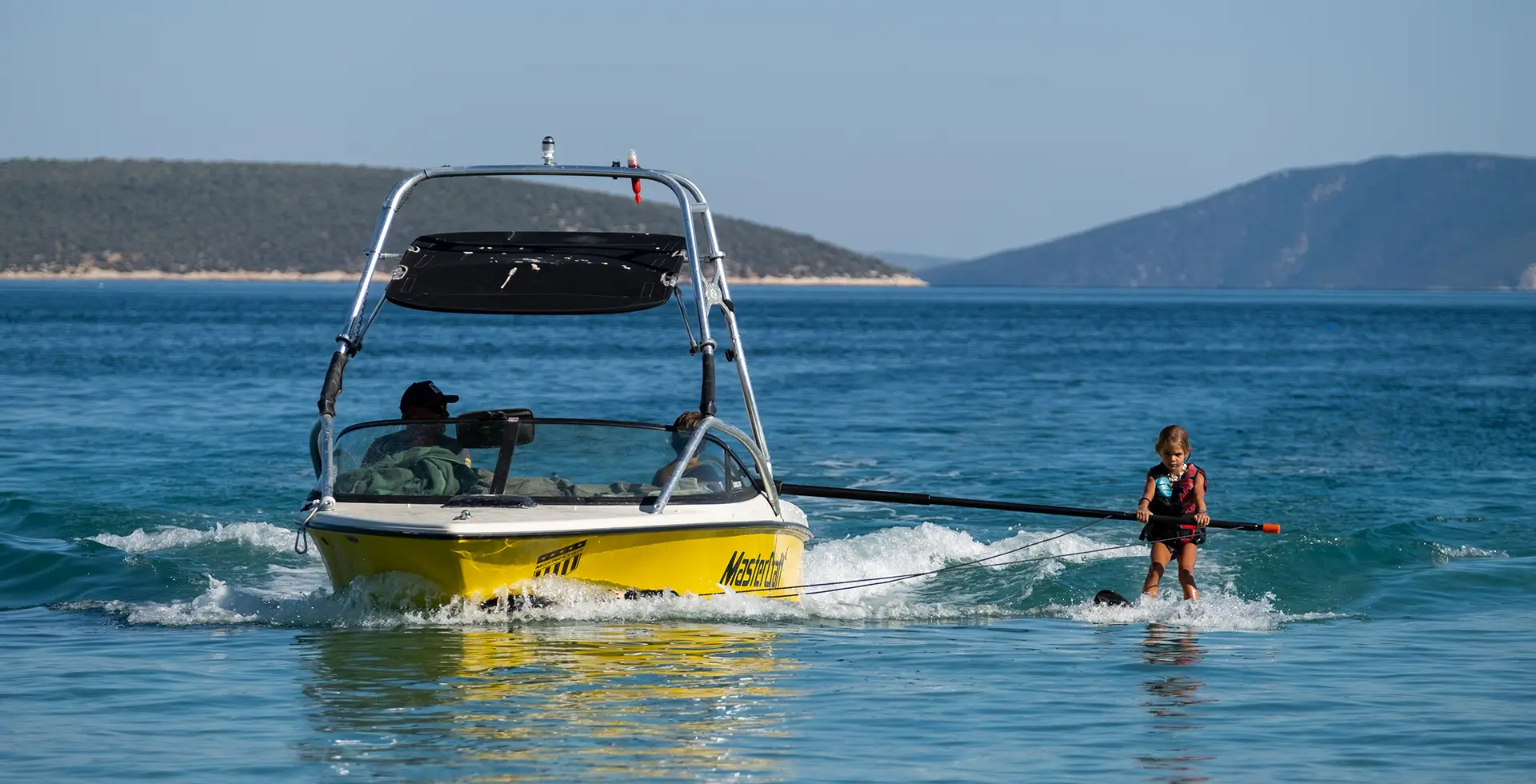 Girl learning to water-skii while holding assistance pole